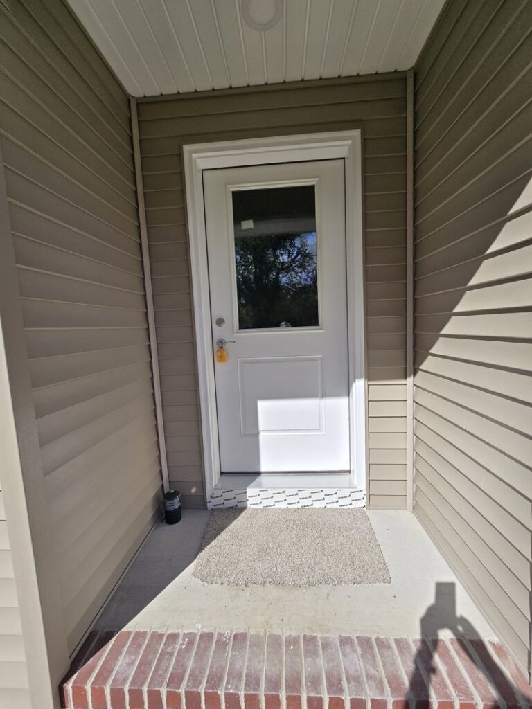 A newly installed white front door with a window and light-colored siding by Shore Home Construction Roofing in Salisbury, MD.