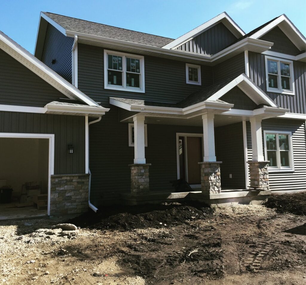 Recently installed gutters and downspouts on a house, with disturbed ground from construction by Gutter Flow7 LLC in Madison, WI.