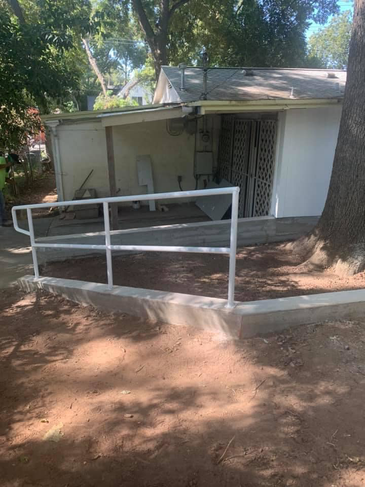 Newly installed white handrail and concrete path next to a building by Valdez Remodeling & Weatherization Inc. in Austin, TX