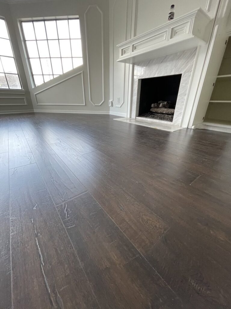 Newly installed dark hardwood flooring and a white fireplace in a living room by AMG Construction Group LLC in Houston, TX.