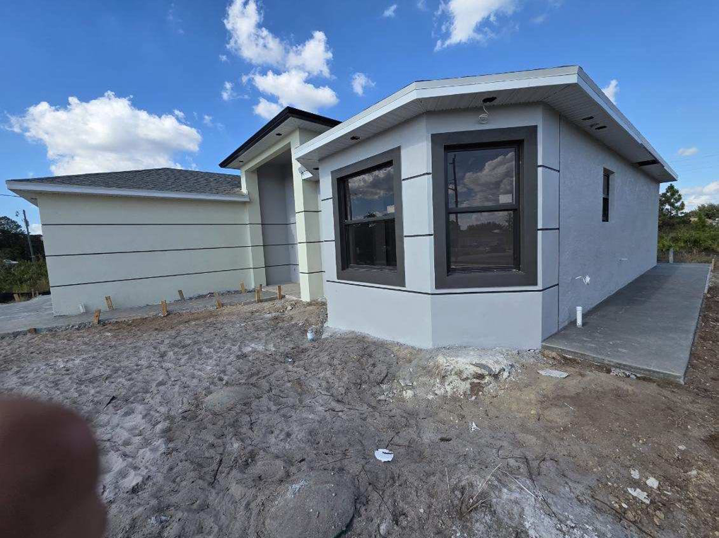 Side view of a new house under construction, featuring bay windows and a concrete walkway by C.A Tano Construction & Appliances Cgc1531664 in Cape Coral, FL.