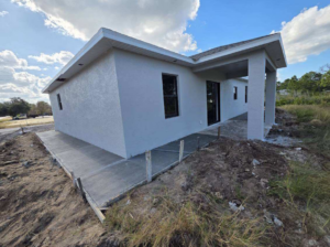 Side view of a new house under construction, featuring a covered patio and concrete walkway by C.A Tano Construction & Appliances Cgc1531664 in Cape Coral, FL.