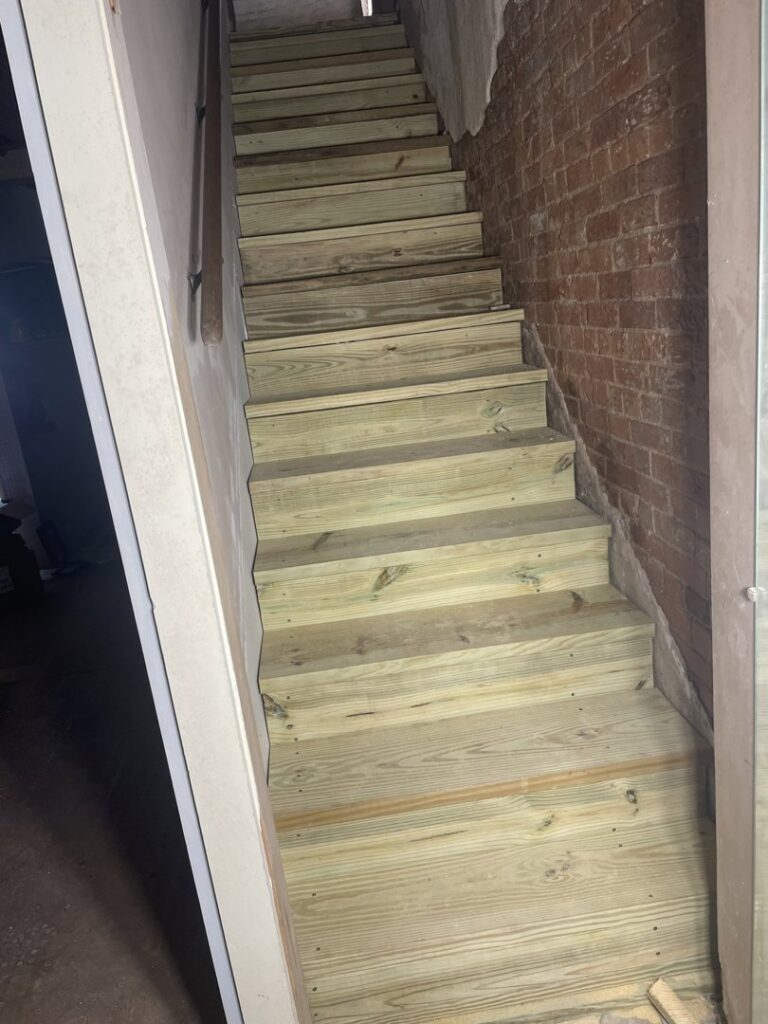 Newly constructed indoor wooden staircase next to a brick wall by CJP Construction handyman services in Pierce, NE.