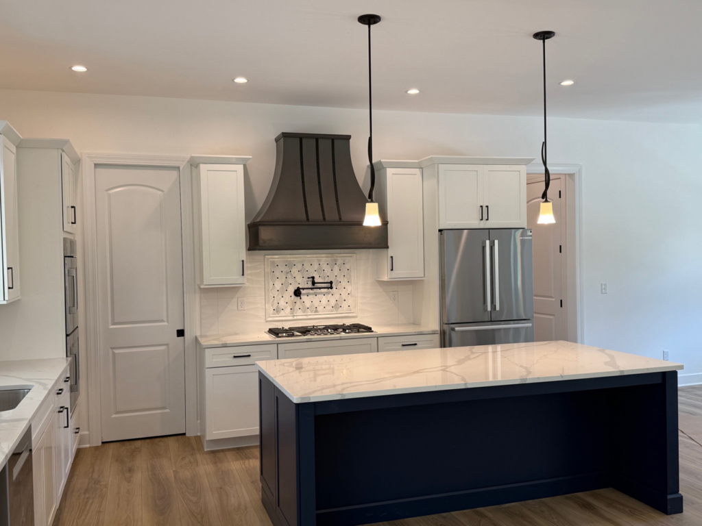 A newly designed kitchen with white cabinets, a dark blue island, and stainless steel appliances by McDonald Custom Homes in Schenectady, NY.