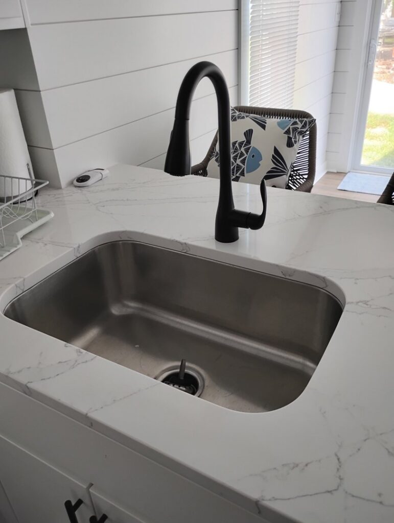 A newly installed modern kitchen sink with a black faucet and white quartz countertop by McCollister Contracting LLC in New Castle, DE.