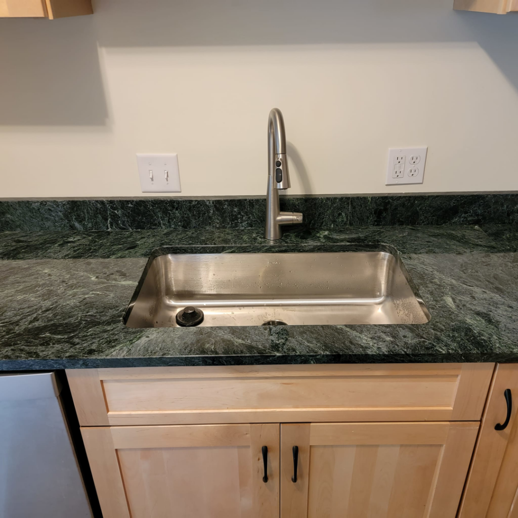 A newly installed kitchen sink and modern faucet with dark green granite countertops by Jonny Hinton - Handyman Extraordinaire in Colorado Springs, CO.