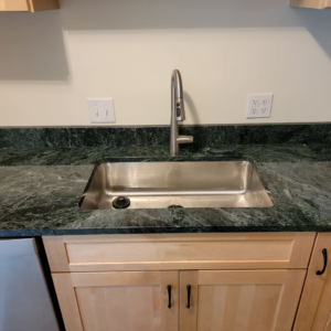 A newly installed kitchen sink and modern faucet with dark green granite countertops by Jonny Hinton - Handyman Extraordinaire in Colorado Springs, CO.