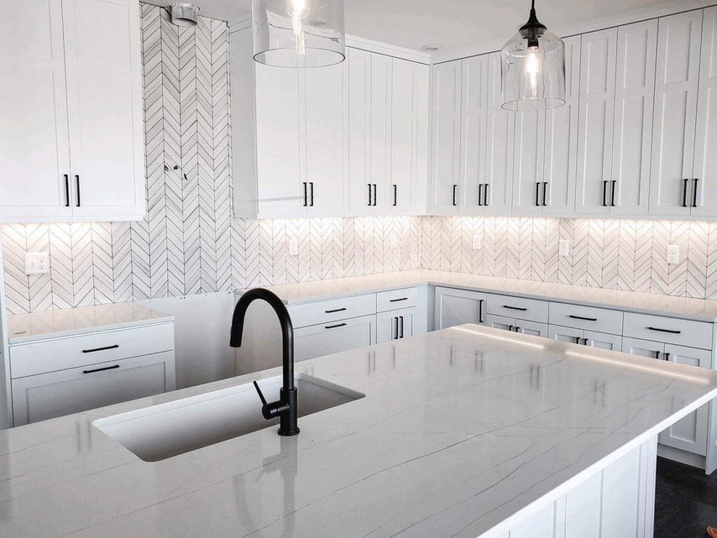 A newly installed kitchen with white cabinets and a herringbone tile backsplash by Brian's Tiles in Duluth, MN.