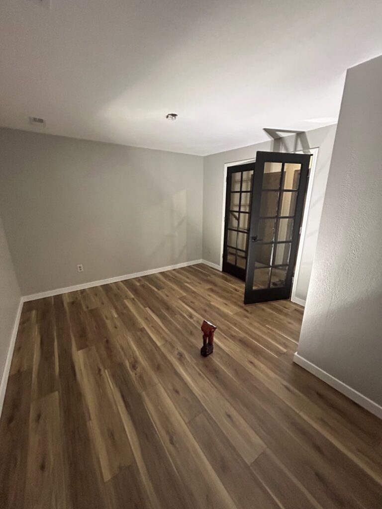 An empty room with new laminate flooring and dark French doors, expertly installed by Dakota Small Jobs in Sioux Falls, SD.