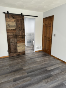 Newly installed laminate flooring and a custom barn door leading to a bathroom by Strausbaugh Construction Services LLC in Cincinnati, OH.