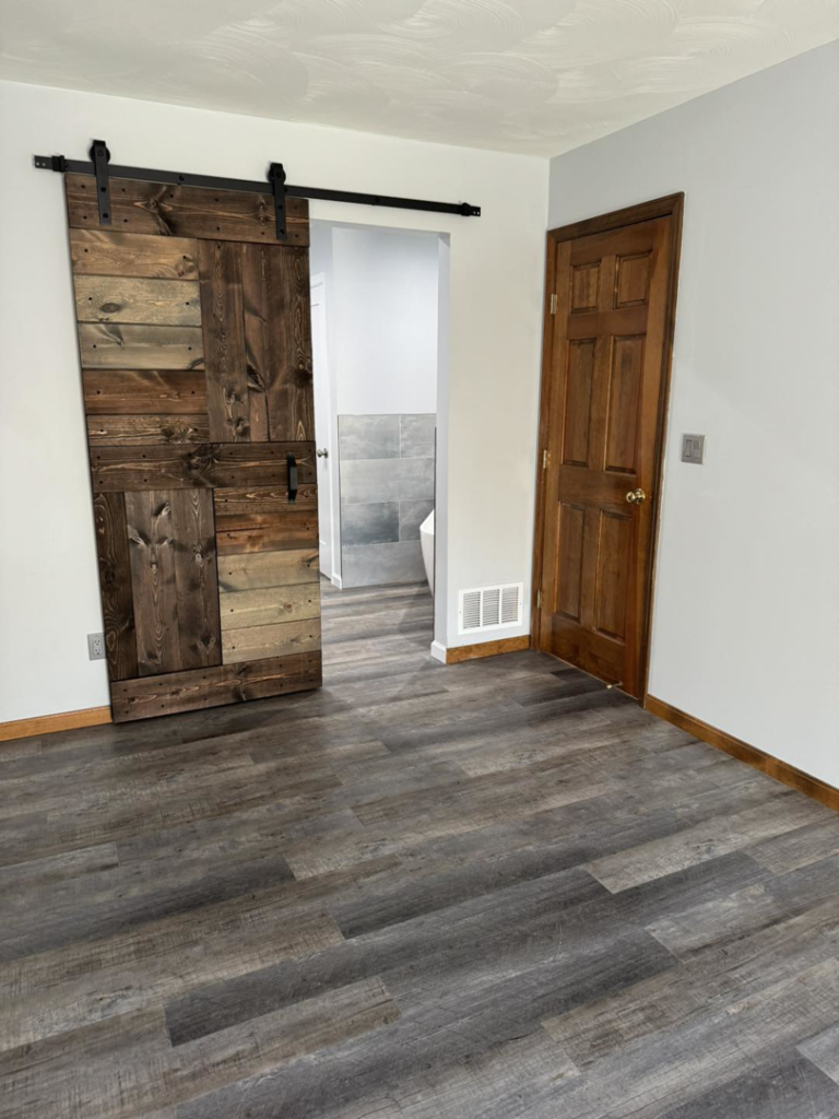 Newly installed laminate flooring and a custom barn door leading to a bathroom by Strausbaugh Construction Services LLC in Cincinnati, OH.