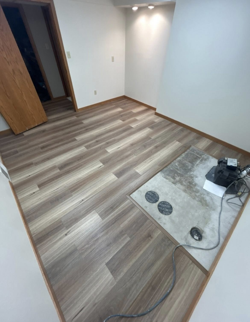 A basement room with newly installed laminate flooring and painted walls by I Need a Guy Handyman Services LLC in Moorhead, MN