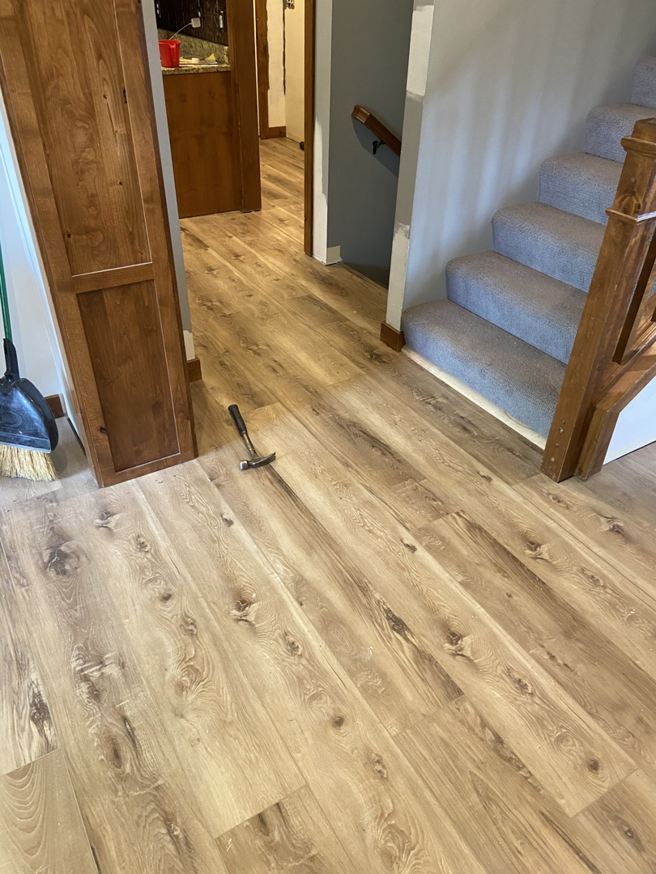 Newly installed laminate flooring in a hallway leading to a carpeted staircase, completed by RT Handyman LLC in Sioux Falls, SD.