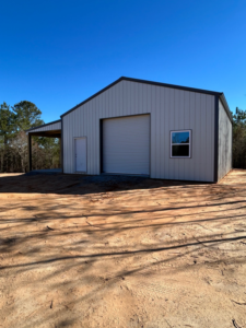 A newly constructed metal barn or building with a roll-up door, regular door, window, and lean-to, by Southern Style Barns & Buildings LLC in Lake Charles, LA.