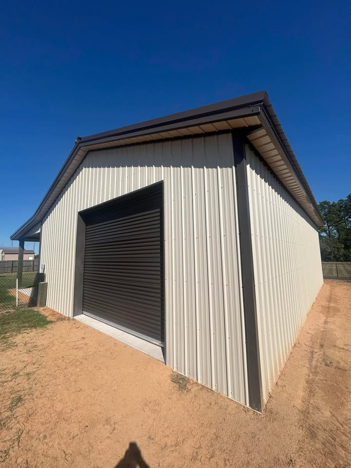 A newly constructed metal barn or garage with a dark roll-up door by Southern Style Barns & Buildings LLC in Lake Charles, LA.