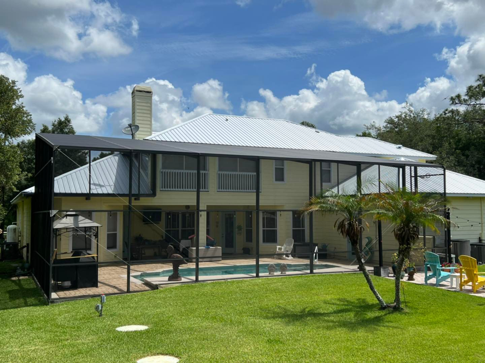 A large yellow house with a newly installed metal roof and a screened-in pool area by Hastings Roofing Service Inc. in Orlando, FL.