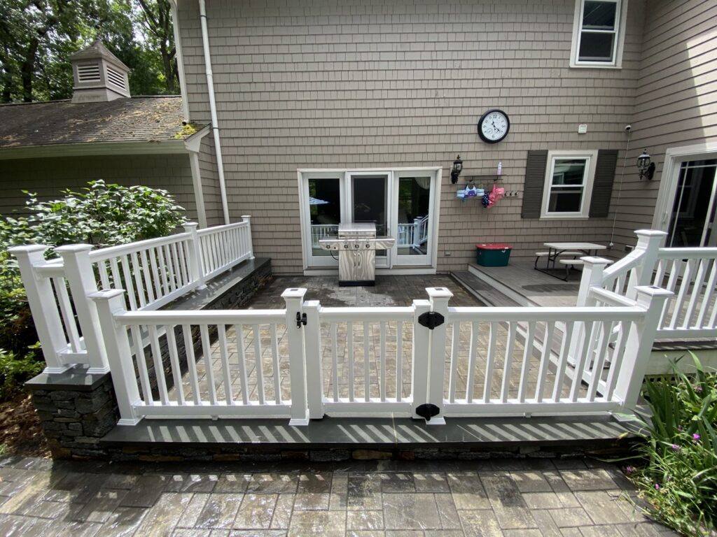 A newly installed patio with white fencing and stone veneer work by Eagle Exteriors in Cumberland, RI.