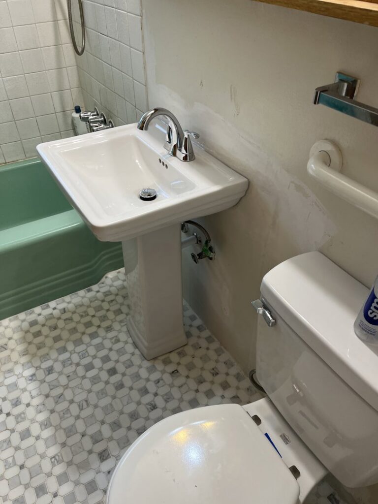 Newly installed pedestal sink and toilet in a bathroom with stylish mosaic floor tiles by Guzmanremodeling LlC in Renton, WA.
