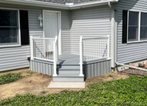A newly installed front porch and deck with white railings and grey siding by Shifting Sands Contracting in Alvordton, OH.