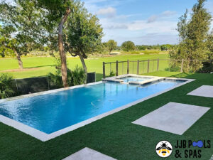 A newly constructed rectangular pool and spa with artificial turf and pavers, offering a golf course view by JJB Pools & Spas in Tampa, FL.