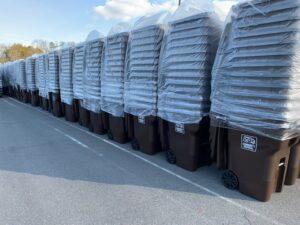 A long line of new, wrapped residential trash bins with the Community Disposal logo, ready for distribution in Jacksonville, FL.