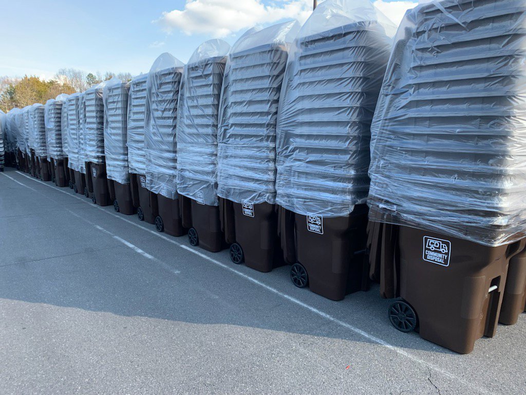 A long line of new, wrapped residential trash bins with the Community Disposal logo, ready for distribution in Jacksonville, FL.