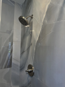 A close-up of a new shower head and control valve installed on grey marble-patterned tiles by AGM Remodeling LLC in Glendale, AZ.