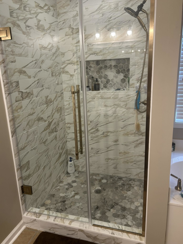 A newly installed shower with a glass door and elegant marble-look tiles by Ingram Painting and Renovation in Birmingham, AL.