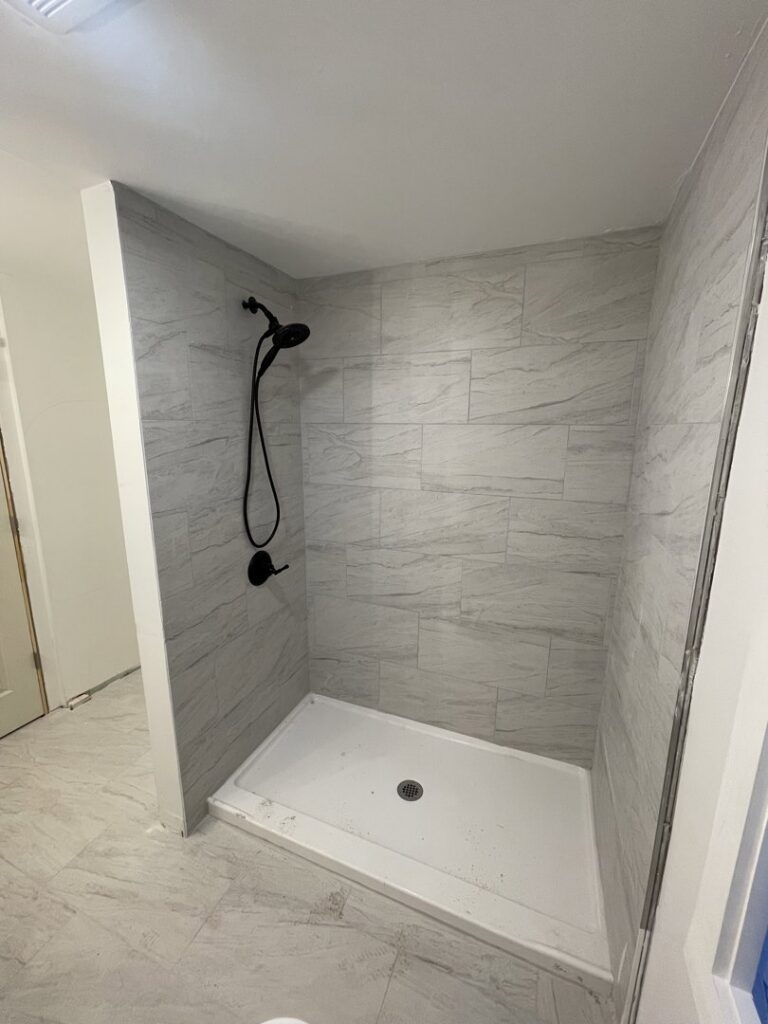 A modern, newly installed shower with light grey tiles and black fixtures by TD Estimating Group LLC in Springfield, MA.