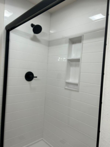 A newly installed shower with white tiles and black fixtures by VanVleet Construction in Brooklyn Park, MN.