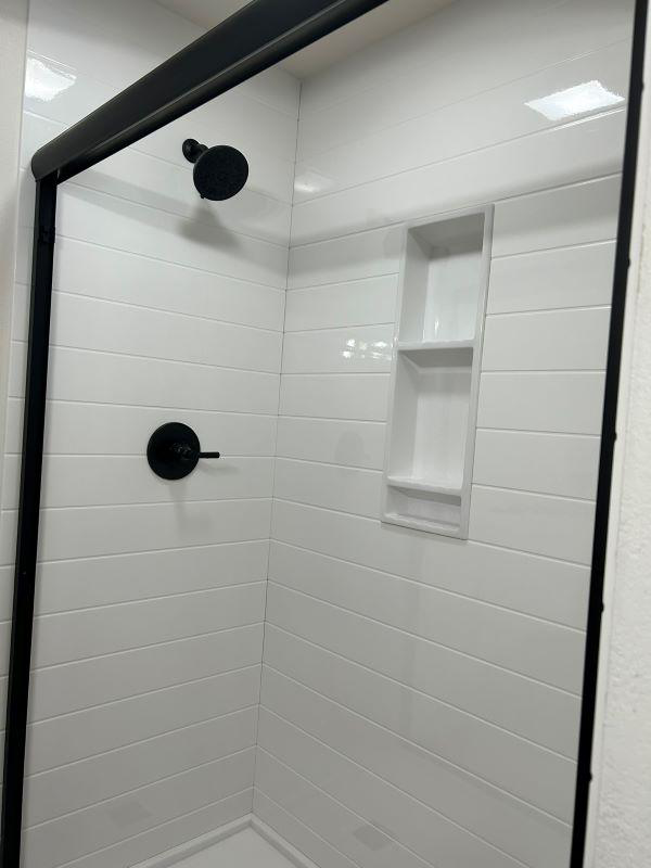 A newly installed shower with white tiles and black fixtures by VanVleet Construction in Brooklyn Park, MN.