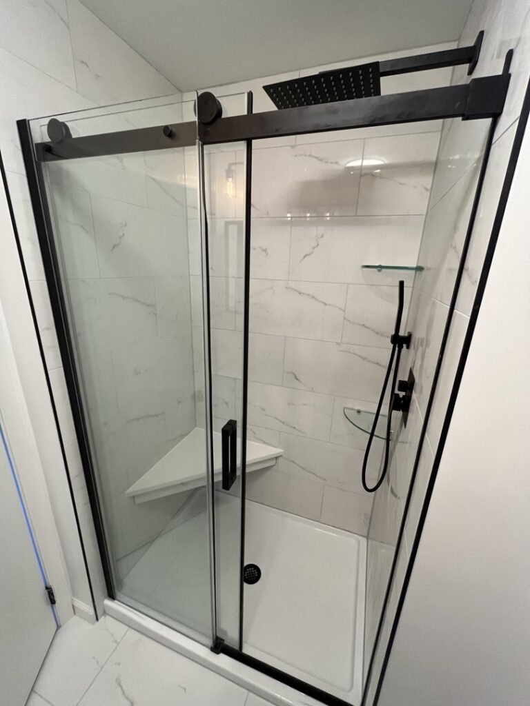A new shower installation featuring white marble-look tiles, a glass sliding door, and a built-in bench by MPH Design in Philadelphia, PA.