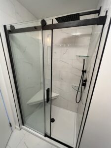 A new shower installation featuring white marble-look tiles, a glass sliding door, and a built-in bench by MPH Design in Philadelphia, PA.