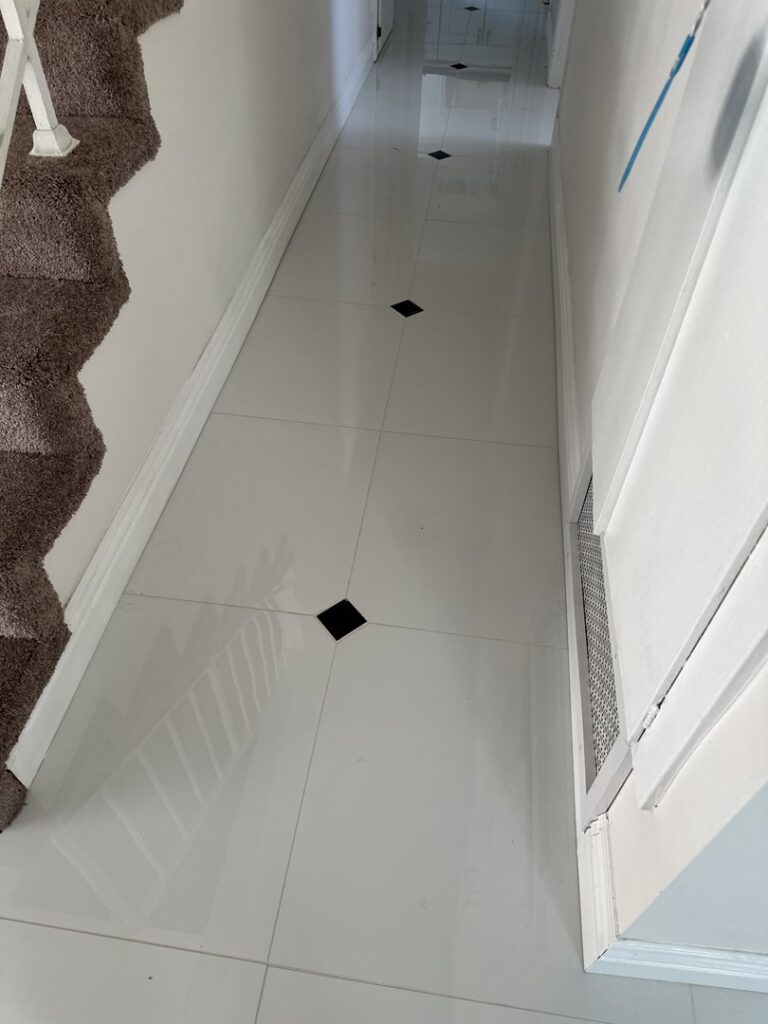 A hallway with newly installed white tile flooring and black accent tiles by Peraza Handyman Services Llc in Bakersfield, CA.