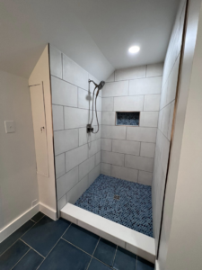 A newly tiled shower with blue mosaic floor and white subway tiles, showcasing a bathroom renovation by Great Home Construction LLC in Annapolis, MD.