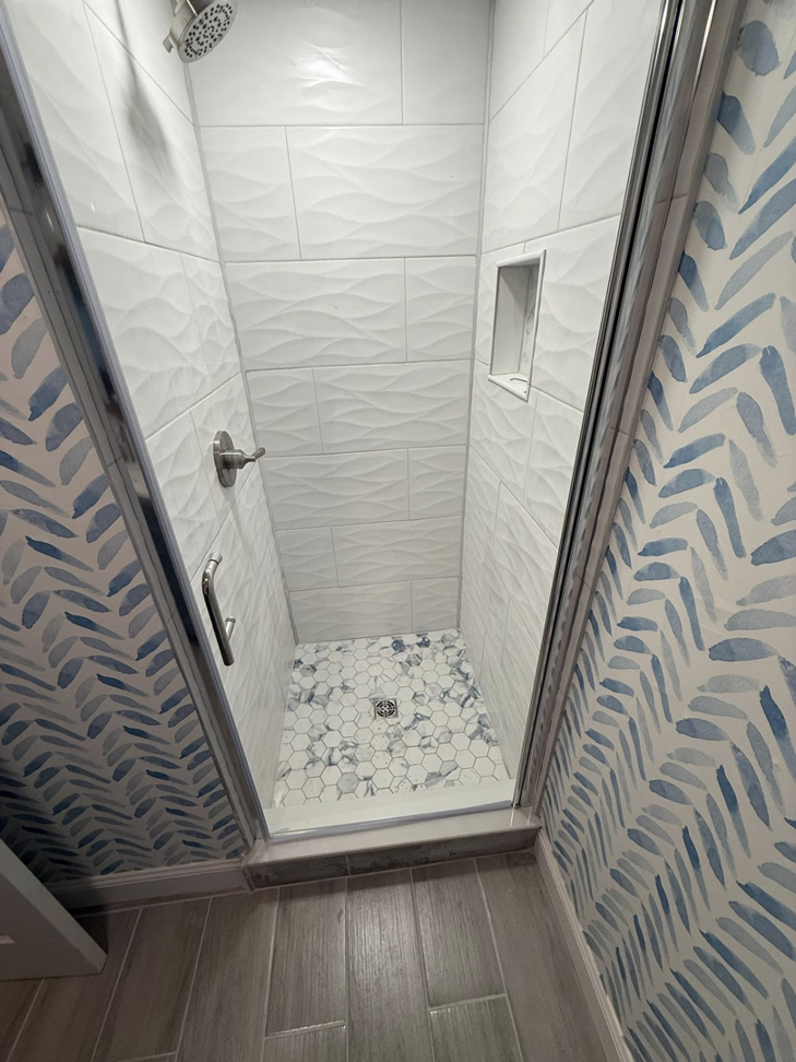 A newly installed tiled shower with a glass door and hexagonal floor tiles by MS Renovation in Boston, MA.