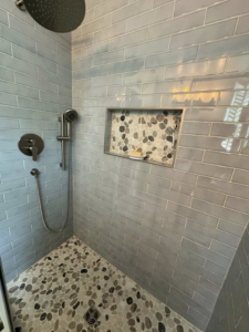 A newly tiled shower with a rain shower head, handheld shower, and a decorative pebble mosaic niche by NC Home Remodeling and Custom Cabinetry in Alexandria, VA.