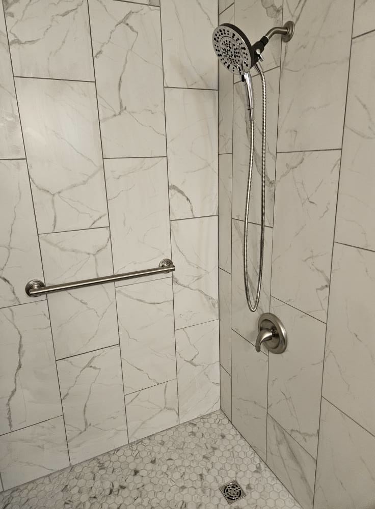 A newly tiled shower with a modern shower head, faucet, and grab bar installed by Tim's handyman service in Cherry Hill, NJ.