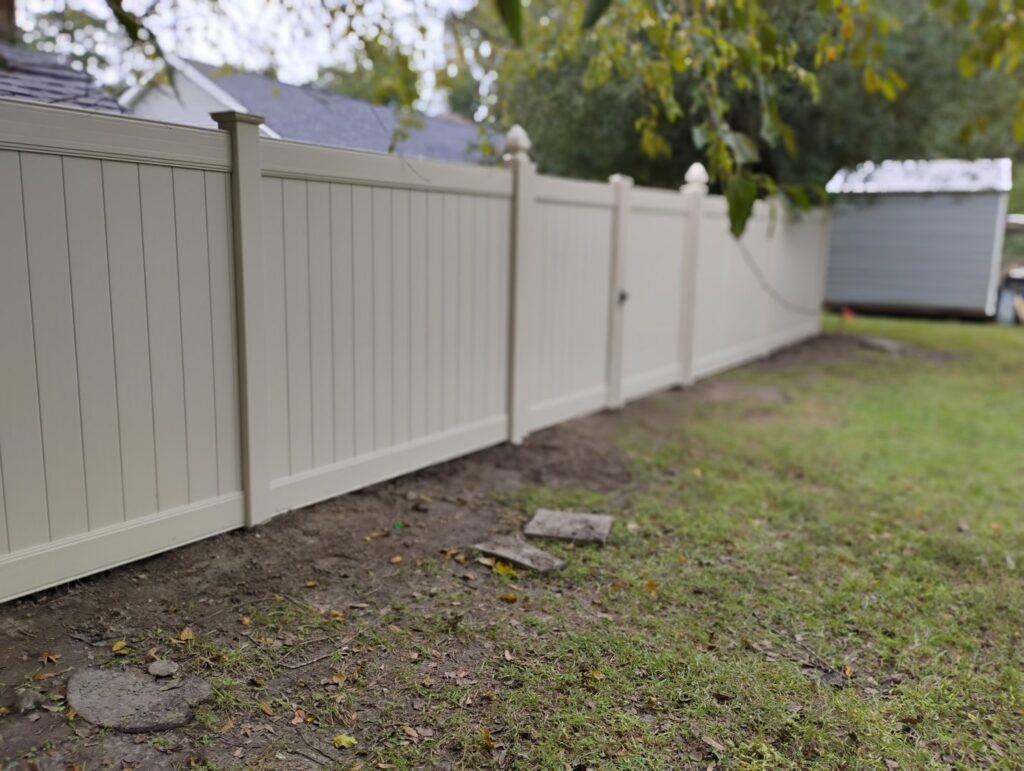 A newly installed light-colored vinyl privacy fence with a gate by Fence & Deck Connection, Inc. in Savannah, GA.