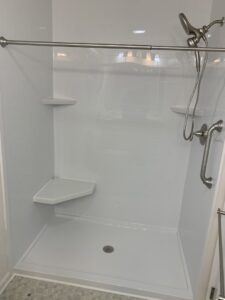 A new white shower installation with subway tile pattern panels, a corner bench, and grab bars by Peninsula Bath & Tile in Salisbury, MD.