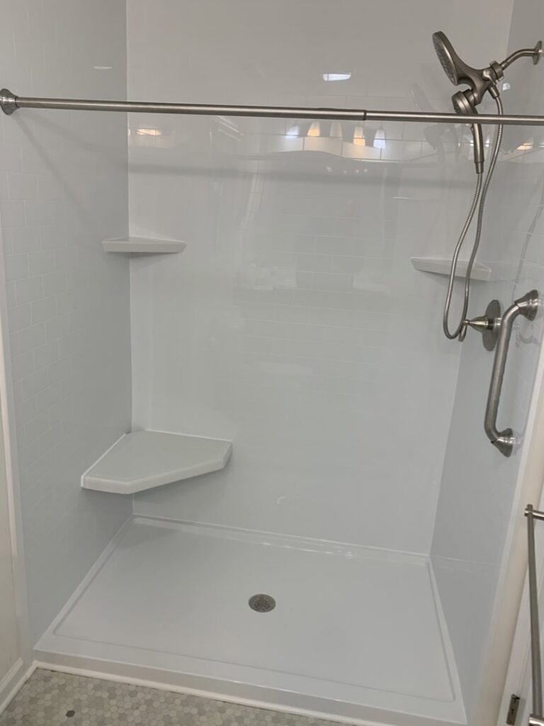 A new white shower installation with subway tile pattern panels, a corner bench, and grab bars by Peninsula Bath & Tile in Salisbury, MD.
