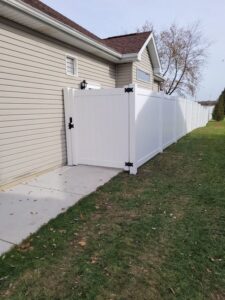 A newly installed white vinyl privacy fence with a gate next to a house by Badger Vinyl Products in Madison, WI.