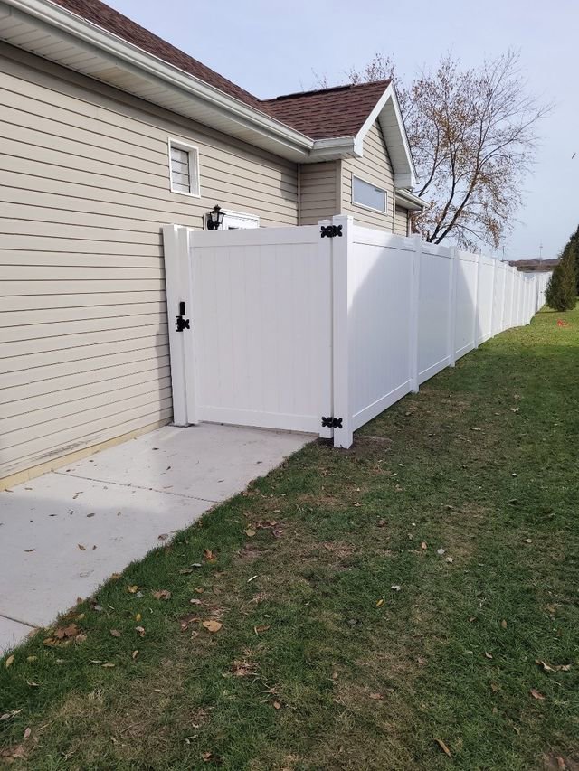 A newly installed white vinyl privacy fence with a gate next to a house by Badger Vinyl Products in Madison, WI.