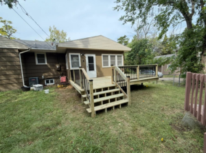 A newly constructed wooden deck with stairs and black railings attached to a house by Bill's Handyman Services in Anchorage, AK.