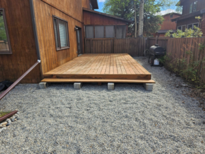 A newly constructed wooden deck on a gravel patio next to a house by Fairbanks Finest Handyman in Fairbanks, AK.