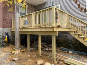 A newly constructed wooden deck with stairs and railings, showing the support structure, built by Men Construction in Lowell, MA.