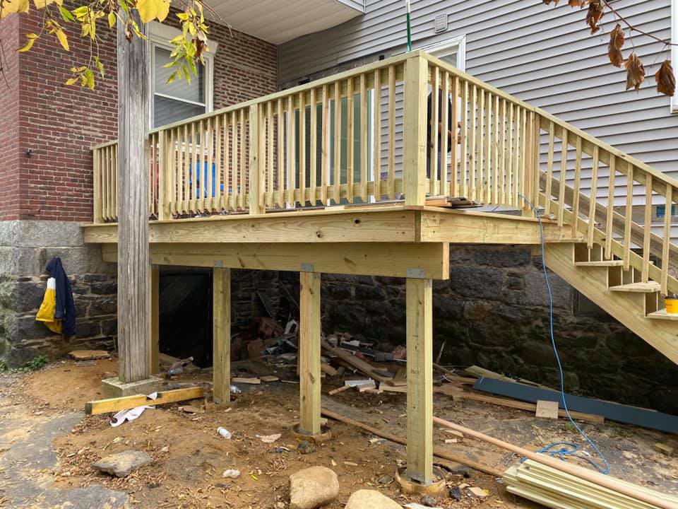 A newly constructed wooden deck with stairs and railings, showing the support structure, built by Men Construction in Lowell, MA.