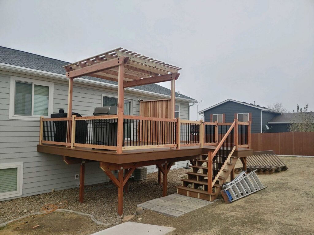 A newly constructed wooden deck with a pergola and stairs attached to a house, showing a completed renovation project by Rapid Renovations LLC in Rapid City, SD.