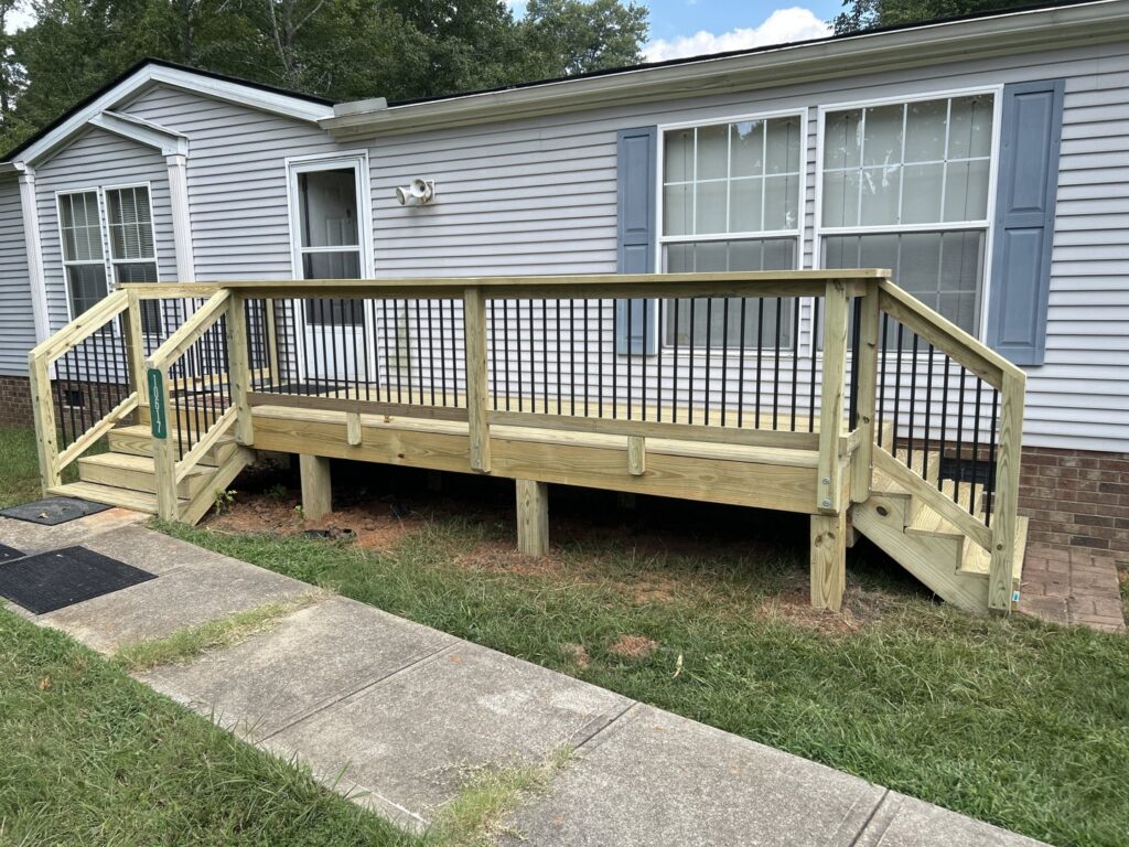 A newly constructed wooden deck with black balusters and stairs leading to a house by Elite Xteriors NC in Cary, NC.