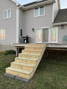 Newly installed wooden deck stairs leading to a house by CJP Construction handyman services in Pierce, NE.
